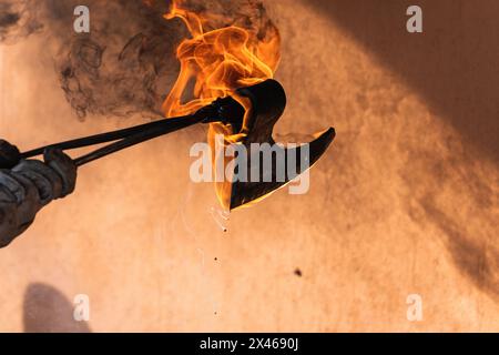 Faceless artisan hardening burning iron sharp weapon in hot water during metal forging process in smithy Stock Photo