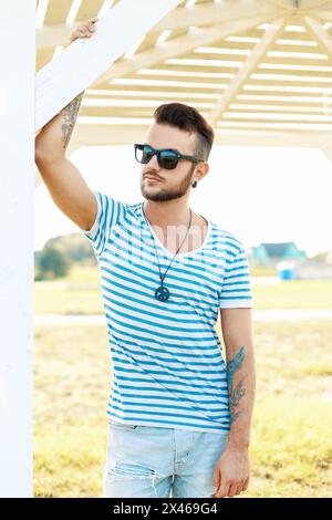 Handsome Hipster Man In Sunglasses With A Tattoo On The Beach On A Sunny Day Stock Photo