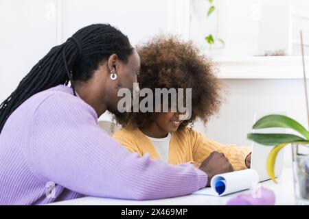 Smiling African American dad sitting at table with girl surfing netbook while preparing task for school Stock Photo