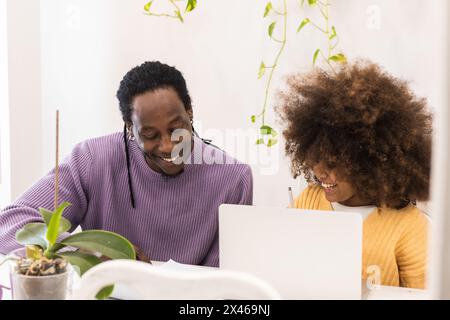 Positive African American dad sitting next to daughter using netbook while doing studies at home Stock Photo