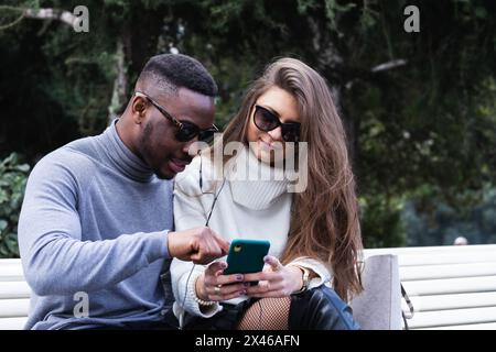 Side view of content adult multiracial couple in love listening music on mobile phone while spending time together in park Stock Photo
