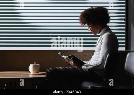 Side view of concentrated young African American male student with curly hair in casual clothes taking notes in copybook while doing homework assignme Stock Photo