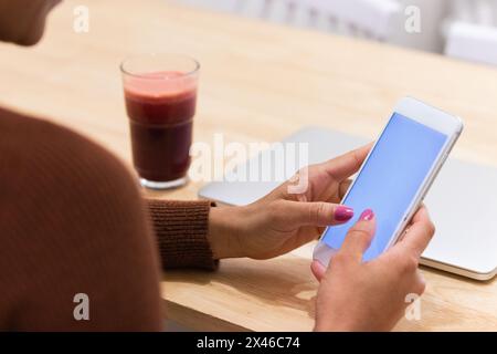 Cropped unrecognizable African American female freelancer browsing smartphone while sitting at table in cafe and working on remote project Stock Photo