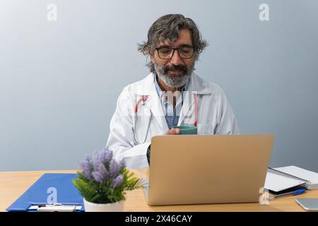 Senior male medic having video call with patient during telemedicine consultation in hospital Stock Photo