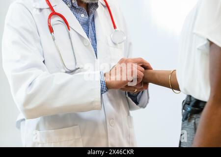 Crop of anonymous senior male doctor measuring pulse of black female patient during check up in hospital Stock Photo