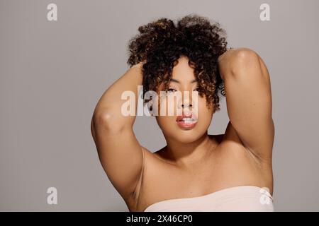 A beautiful young African American woman with curly hair poses gracefully in a studio setting for a portrait. Stock Photo