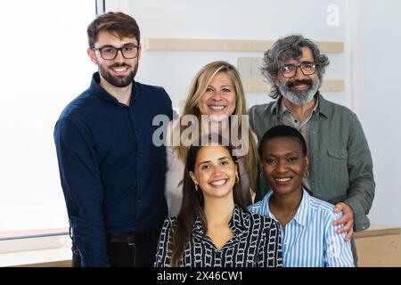 Delighted multiracial female colleagues looking at camera and smiling while sitting in workplace together Stock Photo