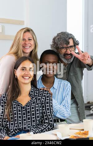 Delighted multiracial female colleagues looking at camera and smiling while sitting in workplace together Stock Photo