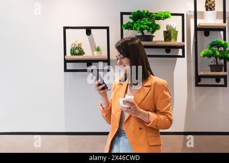 Side view of well dressed female entrepreneur standing in workplace and using mobile phone Stock Photo
