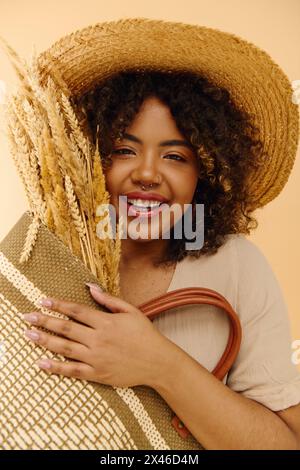 Beautiful African American woman in a summer dress, curly hair cascading, holds a bag while wearing a stylish straw hat. Stock Photo