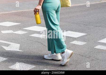 Side view of crop anonymous female with bottle of water walking along crosswalk in city Stock Photo