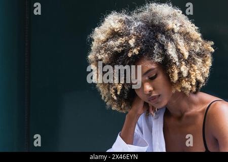 Thoughtful African American female wearing stylish casual outfit looking down while standing against colorful door Stock Photo