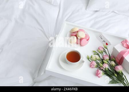 Tasty breakfast served in bed. Delicious macarons, tea, gift box, flowers and I Love You card on tray, space for text Stock Photo