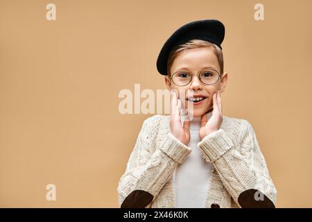 Young boy in glasses and hat, dressed as a film director, against beige backdrop. Stock Photo