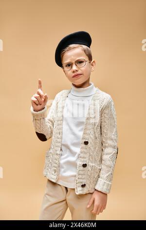 Preadolescent boy in glasses and hat dressed as a film director on beige backdrop. Stock Photo
