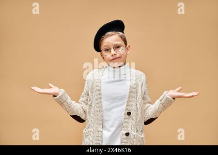 A cute preadolescent boy in glasses and a hat, dressed as a film director on a beige backdrop. Stock Photo