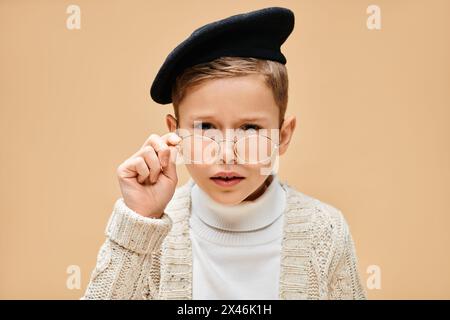 Preadolescent boy in glasses and hat, dressed as a film director on a beige backdrop. Stock Photo