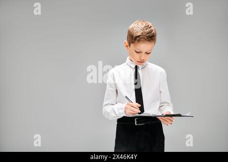 Preadolescent boy in white shirt and tie, focused on writing notes on clipboard. Stock Photo