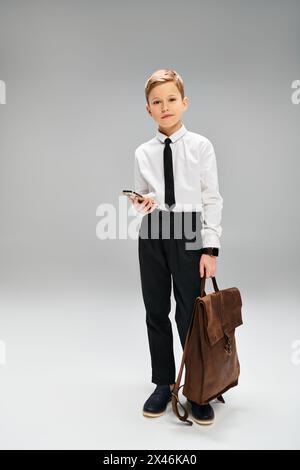 Preadolescent boy in white shirt and tie holds secretive brown bag against gray background. Stock Photo