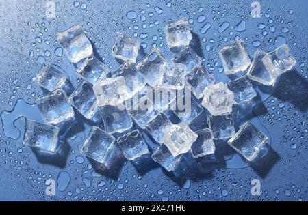 Melting ice cubes and water drops on blue background, flat lay Stock Photo