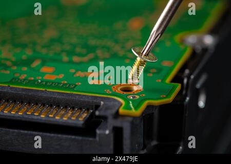 Hard disk drive and printed circuit board with SATA power connector. Magnetic driver torx bit and small machine screw on dark background. Stock Photo