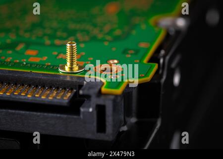 Hard disk drive and printed circuit board with SATA power connector. Magnetic driver torx bit and small machine screw on dark background. Stock Photo