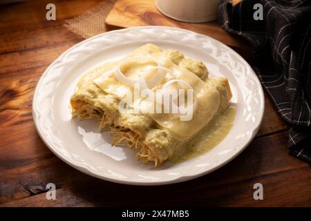 Mexican food. Enchiladas with creamy green sauce filled with shredded chicken meat and covered with melted cheese, in Mexico they are called Swiss Enc Stock Photo