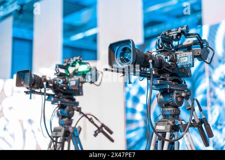 Modern 4K broadcast cameras on a tripod. Big camera mounted on stands at a conference or event Live stream ready, professional video stream. Stock Photo