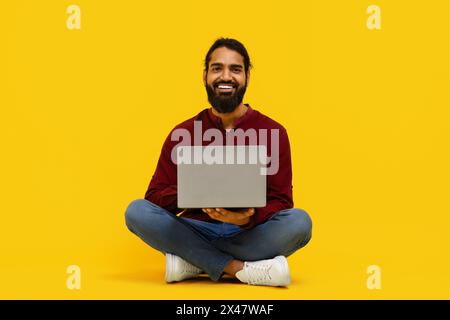 Man Sitting on Floor With Laptop Against Yellow Background Stock Photo