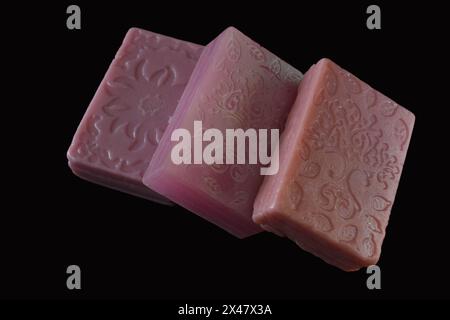 On a black background lie square purple colored bars of soap made at home with drawings on the surface. Stock Photo