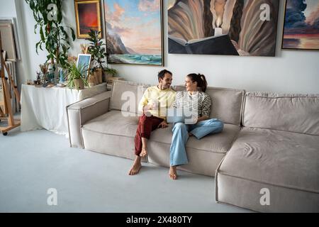 Happy man and woman resting on sofa joyfully laughing chatting talking spending free time together Stock Photo