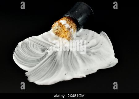 On a black background, shaving foam and an old shaving brush smeared on the surface. Stock Photo