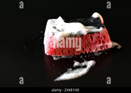 On a black background there is a dish sponge with white soap foam. Stock Photo