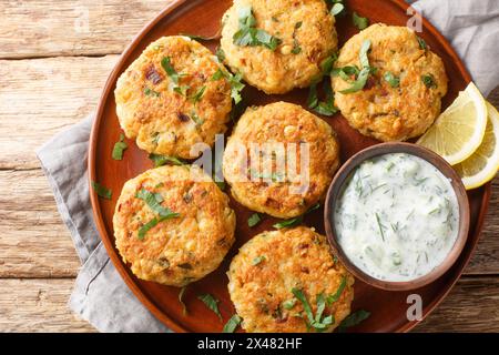 Homemade spicy chickpea pancakes with tzatziki sauce close-up in a plate on a wooden table. Horizontal top view from above Stock Photo