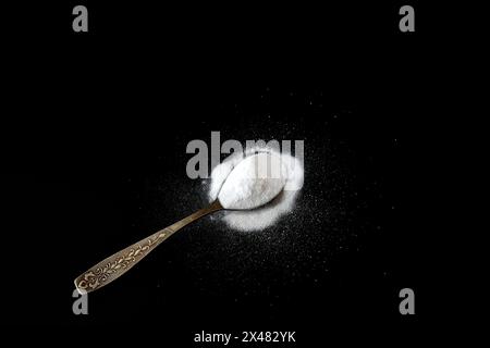 White powder, baking soda poured into a metal spoon lies on a black background. Stock Photo