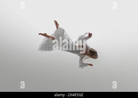 Woman dressed in vintage white gown suspend in mid-air, her long blonde hair cascading around her against white studio background. Stock Photo