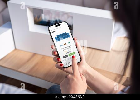 Woman purchases blue sofa online via smartphone from living room, showcasing modern ecommerce app and intuitive user interface design Stock Photo