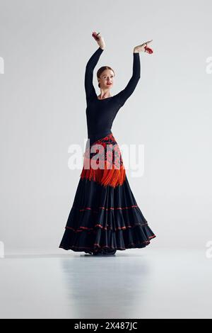 Moment of flamenco magic. Elegant woman in stylish dress standing in eye-catching pose, performing flamenco against grey studio background Stock Photo