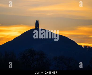 A figure silhouetted in the doorway of distant Glastonbury Tor on the Somerset Levels UK at sunrise Stock Photo