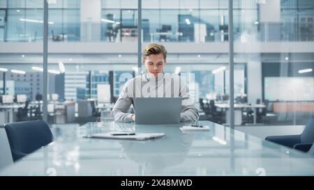 Successful Handsome Businessman Working on Laptop Computer in Big City Office. Finance Investment Analyst Checking Analytics from Project Management Reports, Answering Emails, Checking Social Media. Stock Photo