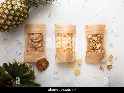 Packages with dried sweet pineapple slices and circles on light background with raw pineapple fruit. Stock Photo