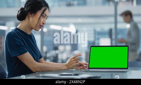 Multiethnic Office Meeting Room: Creative Asian Entrepreneur Female Use Laptop and Pointing on Green Screen Mock Up Display. Stock Photo