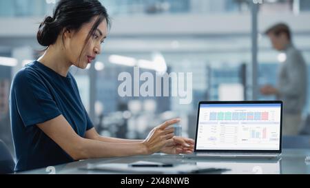 Multiethnic Office Meeting Room: Creative Asian Entrepreneur Female Use Laptop and Pointing on Screen with Financial Plan, Charts, Data. Stock Photo