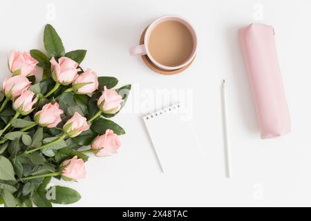 Bouquet of pink roses, notebook and workspace accessories on a white table. Flat lay with blank copy space. Stock Photo