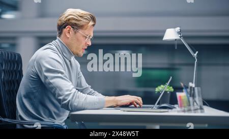Modern Office: Portrait Businessman Sitting at His Desk Working on a Laptop Computer. Man working with Big Digital Data e-Commerce. Energetic day with Blurred Motion background Stock Photo
