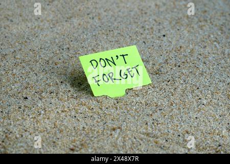 Green sticky notes with word don't forget on top of sand Stock Photo