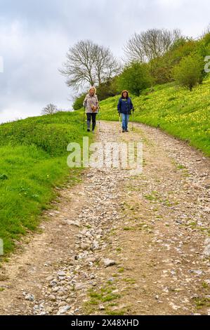 Two middle-aged women walking down a steep gravel road on a grassy hill in South Downs National Park near Amberley in West Sussex, England. Stock Photo