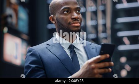 Portrait of Successful African-American Businessman using Smartphone on Street of the Business District in City. Black Digital Entrepreneur uses Mobile Phone e-Commerce App for Stock Market Investment Stock Photo