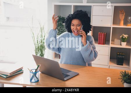 Portrait of pretty young lady wear sweater scream communicate phone laptop desk home office indoors Stock Photo