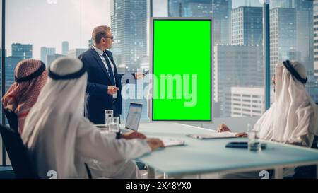 International Manager Holds Meeting Presentation for Saudi Business Partners. Specialist Uses Whiteboard with Vertical Green Screen Mock Up Display. Saudi, Emirati, Arab Office Concept. Stock Photo